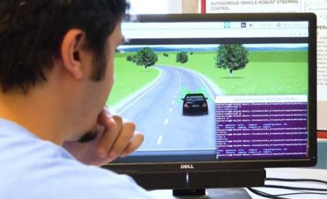 A student looking at a computer monitor showing a simulation of a car driving.