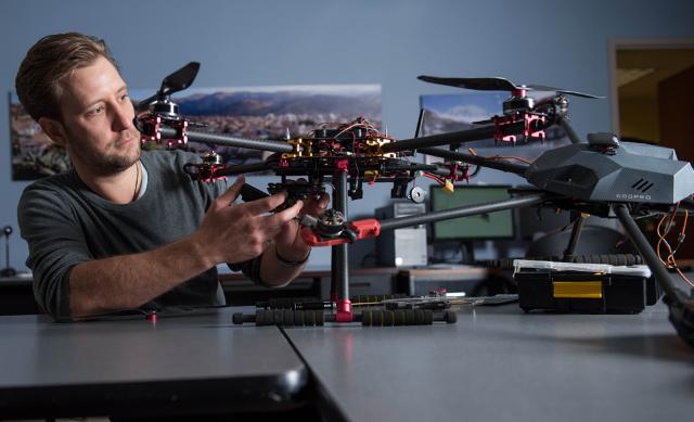 A person working on a drone, with parts and tools scattered around the table.