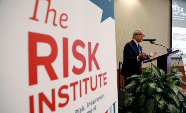 Presenter speaking with a sign that reads "The Risk Institute" in the foreground.