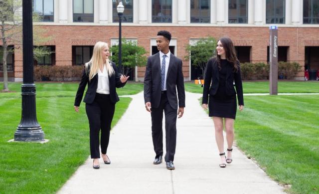 Three students dressed in business professional attire talking and walking together.