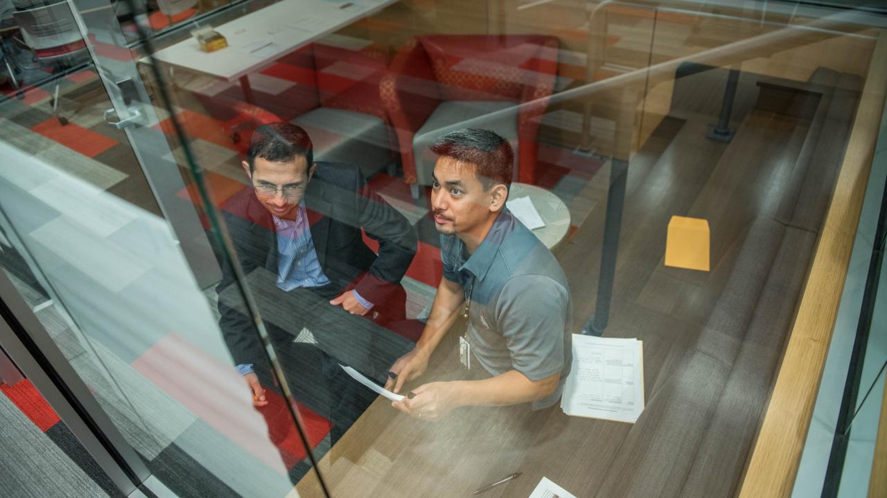 Two people working on a task behind a glass wall.