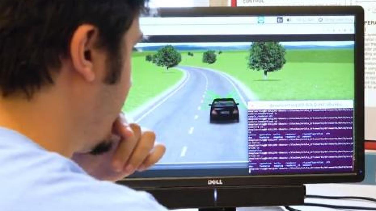 A student looking at a computer monitor showing a simulation of a car driving.