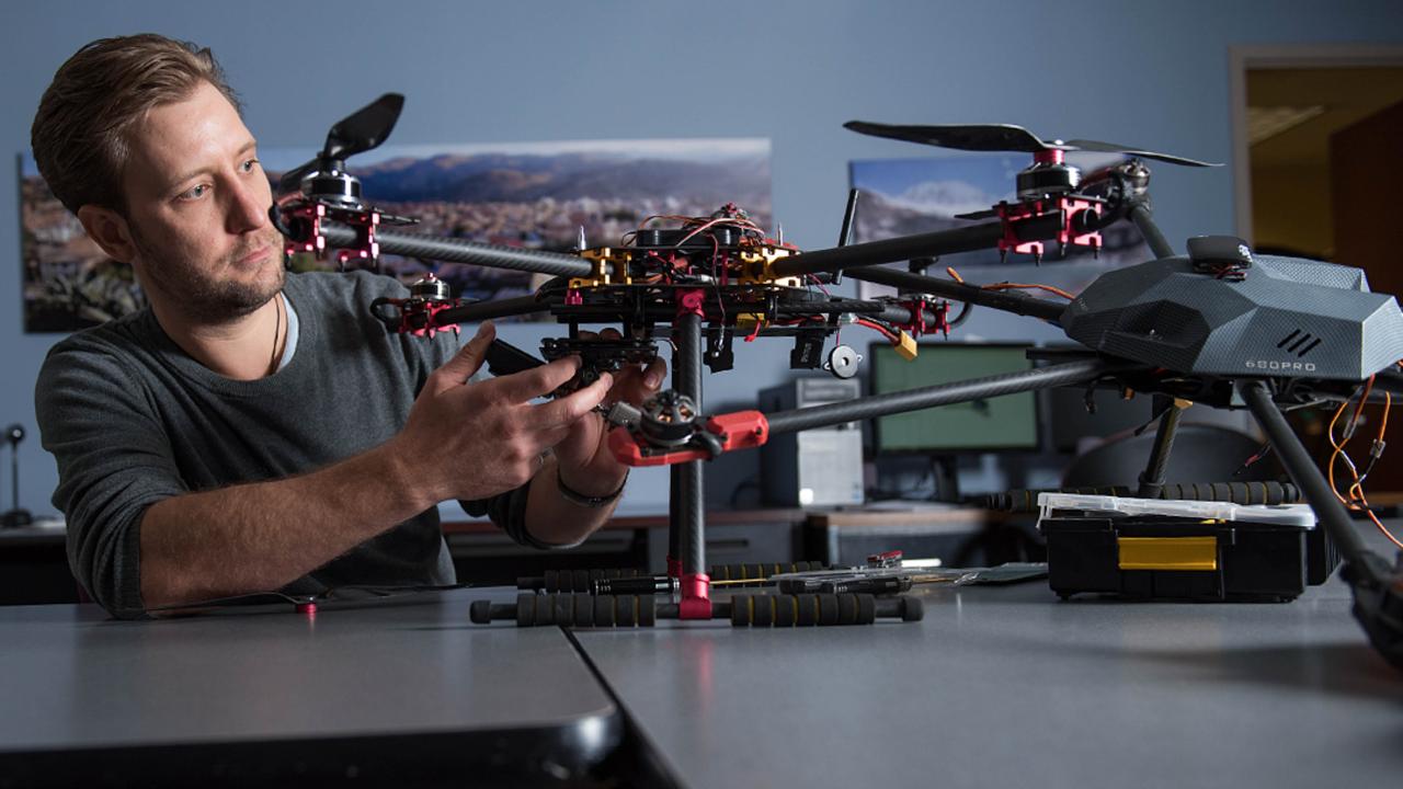 A person working on a drone, with parts and tools scattered around the table.
