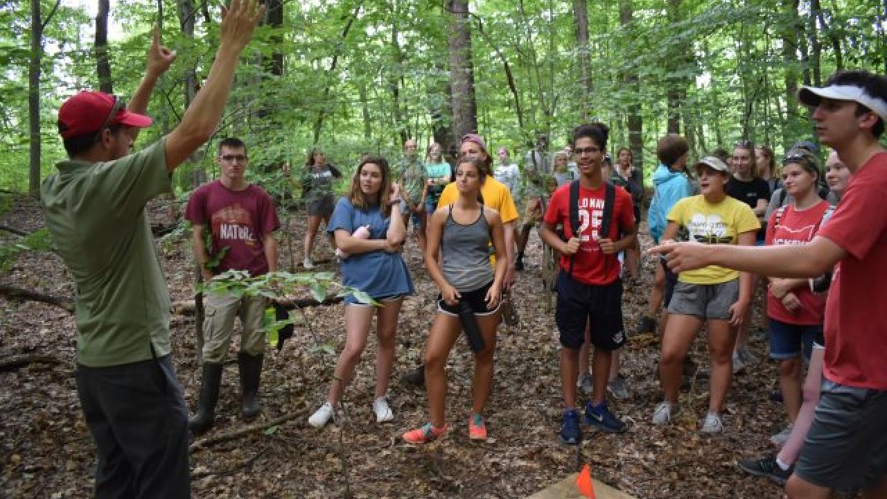 Students listening to an instructor speak during a sustainability research trip in the woods.